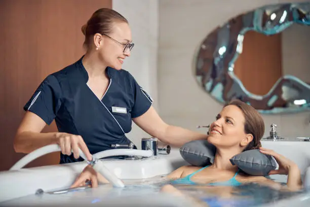 Young female therapist smiling at her patient during the hydrotherapy procedure in a spa salon