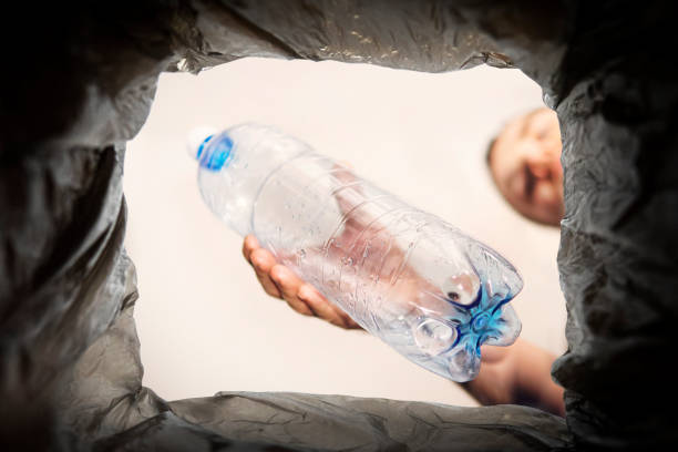 concept du problème de l’élimination des déchets plastiques. un homme jette une vieille bouteille usagée dans une poubelle noire. déchets de bouteilles en plastique, pour le recyclage - toxic substance spilling pouring bottle photos et images de collection