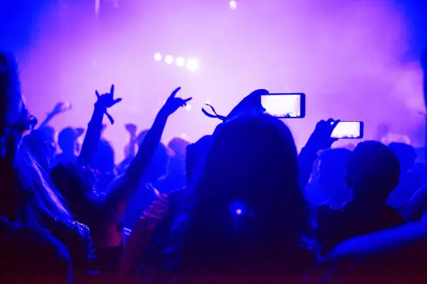 Photo of Raised arms holding smart phones to recording a live concert