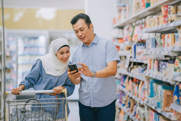 malay couple shopping using smart phone checking shopping list at dairy products section in supermarket during weekend malay couple shopping using smart phone checking shopping list at dairy products section in supermarket during weekend malay couple stock pictures, royalty-free photos & images