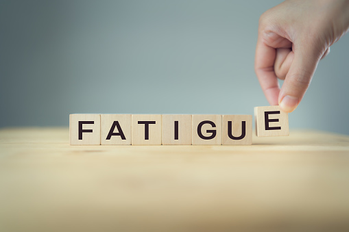 The hand puts a wooden cube with the letter E from the word Fatigue. The word is written on wooden cubes standing on the wooden  table on gray background. Target of difficult situation stress concept