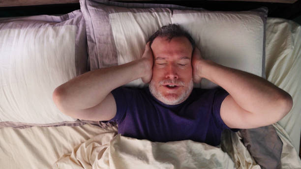 Mature man in bed trying to block out a loud noise outside with his hands Mature man in bed trying to block out a loud noise outside with his hands. He just wishes he could sleep. one mature man only audio stock pictures, royalty-free photos & images
