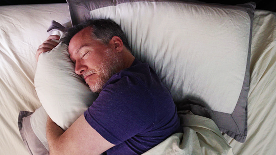 Mature man in bed hugging his pillow with a satisfied expression.