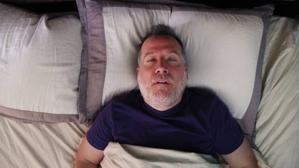 hombre maduro en la cama durmiendo bocanando bocanada con la boca abierta - roncar fotografías e imágenes de stock