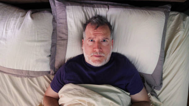 Mature man in bed struck with insomnia looking at camera with frustration stock photo