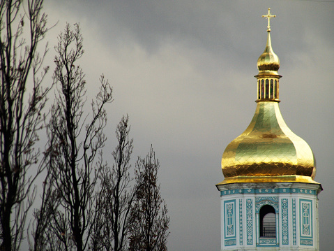 Grey, bleak clouds and deciduous trees with a tower at St Michael's Golden-Domed Monastery in Kyiv.