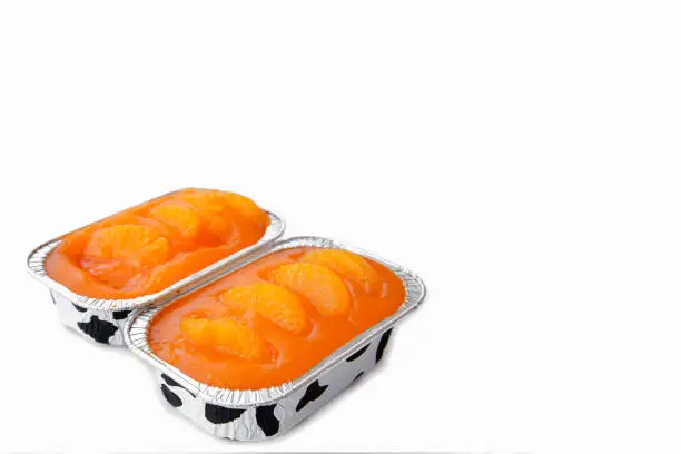 Fresh baked sweet and delicious mandarin orange sponge cake decoration with orange jelly sauce and orange pulp in aluminum foil loaf put on wood table in side view. Homemade bakery concept for cafe