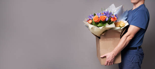 istock White male courier holding a large box with several bouquets. Delivery concept. 1321067936