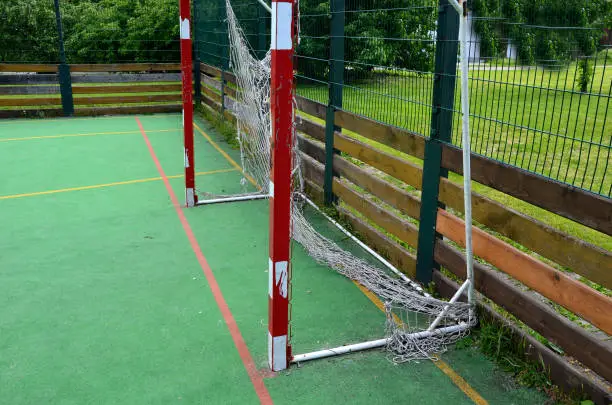 multifunctional outdoor playground for ball games at school. green artificial turf from a plastic carpet with lines. basketball hoops and soccer goals. around the grabbing high net and guardrails