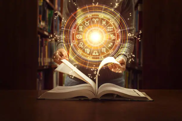 Photo of Woman reading a astrology book. Astrological wheel projection, choose a zodiac sign. Trust horoscope future predictions, consulting stars. Power of universe, astrology esoteric concept.