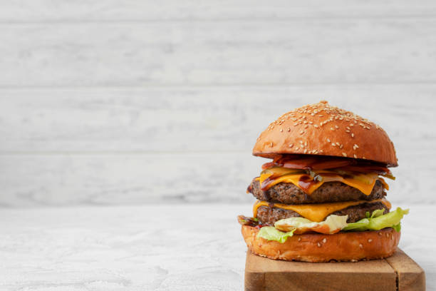 istock Double cheeseburger served on wooden board against white blurred background 1321073270