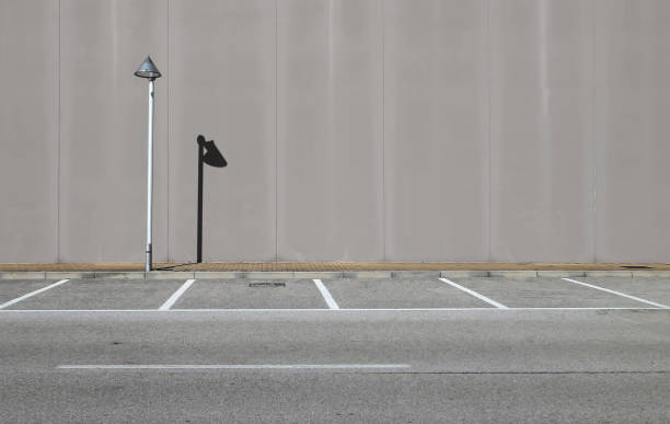 muro di cemento grigio con un lampione e la sua ombra. marciapiede e strada asfaltata con parcheggio di fronte. - sidewalk concrete textured textured effect foto e immagini stock
