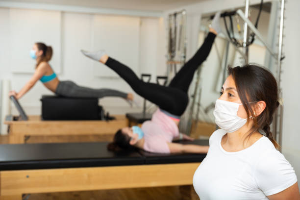 masque de protection de femme faisant des exercices de pilates se démentant sur des machines pilates - pilates machine photos et images de collection