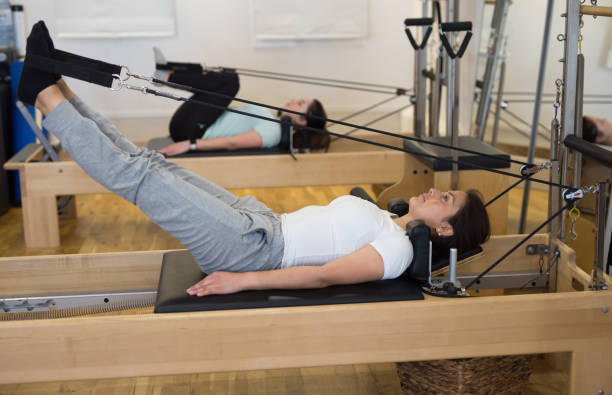 femmes faisant des exercices de pilates mentant sur des machines pilates - pilates machine photos et images de collection