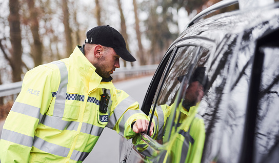 Male police officer in green uniform checking vehicle on the road.