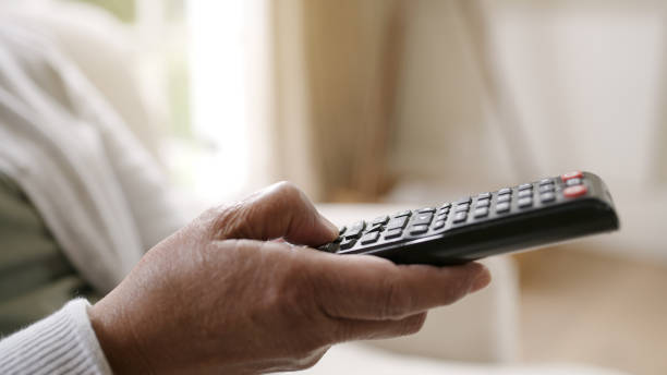 Shot of a woman holding a tv remote while relaxing at home Relaxing some with good TV seniors tv off stock pictures, royalty-free photos & images