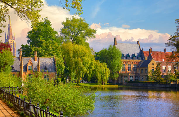 Vintage building over lake of love in Minnewater park in Bruges Belgium near Beguinage monastery of Beguines. Picturesque landscape with green trees sunset time.