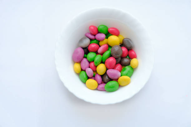 Glazed peanuts of different colors on a plate, white background. Multicolored peanuts. close-up. Snack colored kernel, hazelnut, nut.