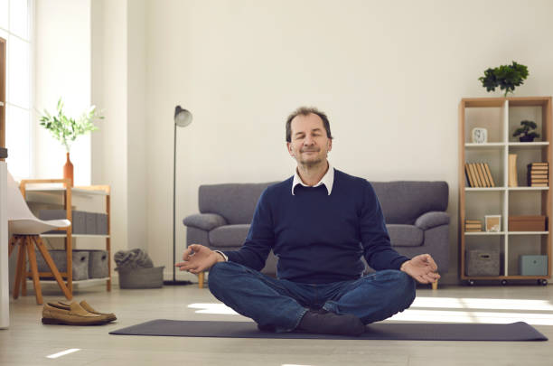 Man sitting on floor, meditating and enjoying moment of peace during busy work day Relaxed man meditating with eyes closed sitting legs crossed on floor rug at home. Happy worker taking a break, feeling calm and enjoying peaceful moment during busy working day at business office meditation room office stock pictures, royalty-free photos & images