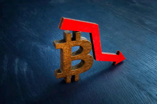 Photo of Bitcoin sign and falling arrow. The crisis and the decline in the price of cryptocurrency.