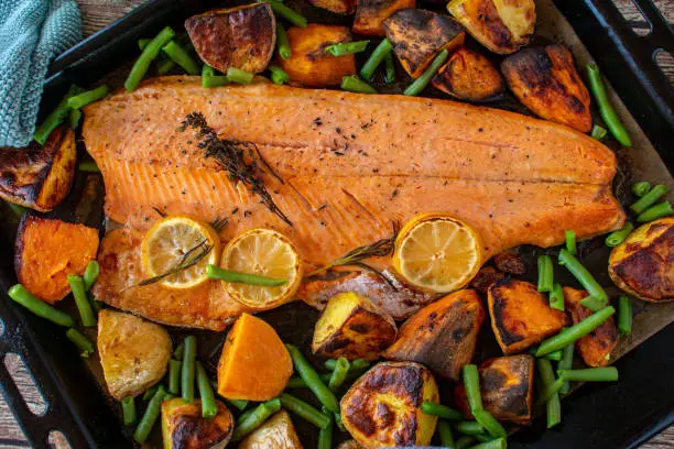 Oven baked grilled salmon filet with green beans served with roasted sweet potatoes and white potatoes on a baking tray. Overhead and closeup view