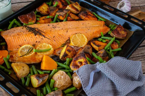 Healthy fish dish with oven grilled salmon fillet and roasted sweet potatoes and white potatoes served with green beans on a baking sheet