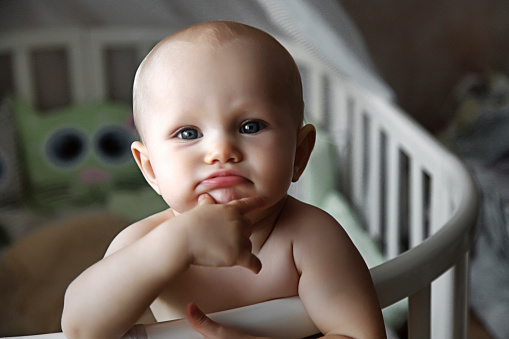 Small cute charming baby looking directly at camera with interest from her crib. Child emotion concept. Copy space