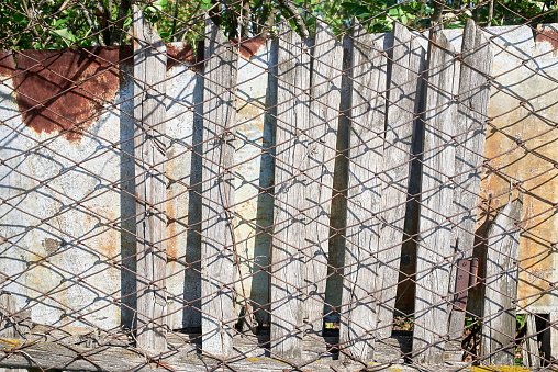 An old wooden fence covered with rusty chain-link mesh. Close-up