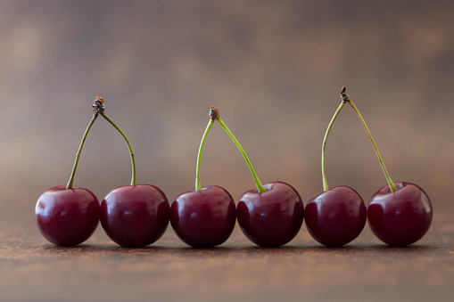 Close Up Group Of Red Sweet Sour Cherries With Stems Isolated On Brown Background, Copy Space, Summer Harvest, Cherries In A Row