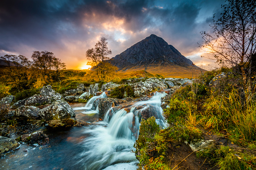 Beautiful landscape in Scotland. Buachaille Etive Mor, known in Gaelic as The Great Herdsman of Etive, a pyramid shaped mountain. Watefall formed by river Etive in the foreground. Beautiful sunset sky with Colourful clouds. Scotland - UK