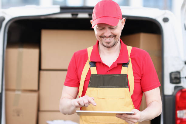 istock Male courier in uniform stands near car with boxes and holds tablet 1321097718