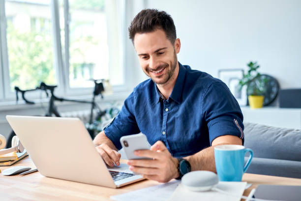 istock Young man working at home with laptop messaging on smartphone 1321100639