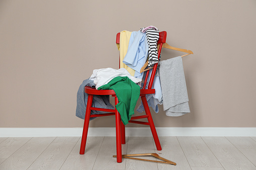 Different clothes on red chair and hangers near light grey wall