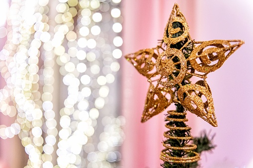 Close-up of Christmas star - gold tree topper and illuminated defocused garland in the background.