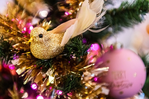 Close-up of Christmas decorations - golden glittering bird on a Christmas tree. Beautiful Christmas ornaments, Christmas pink bauble, golden chain and pink Christmas lights.