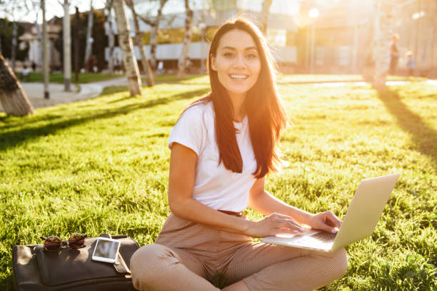 istock Beautiful woman sitting on grass outdoors using laptop computer. 1321110147
