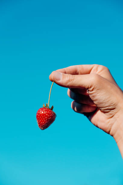 istock man holds a strawberry against the sky 1321110824