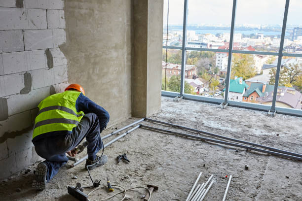 istock Builder in workwear and safety helmet is installing plastic pipes in flat of building under construction with panoramic windows. High-rise house 1321114652