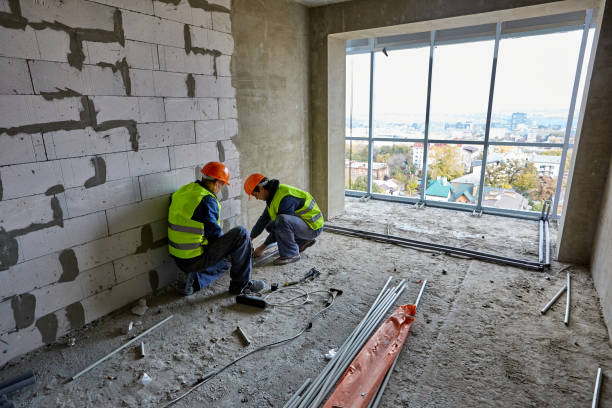istock Two men builders in workwear and hardhats installing plastic pipes using modern tools in flat of building under construction with panoramic cityscape 1321114813