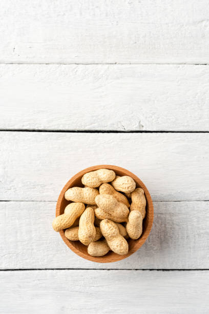 istock Tasty peanuts in bowl on white wooden background with copyspace. Top view 1321117015