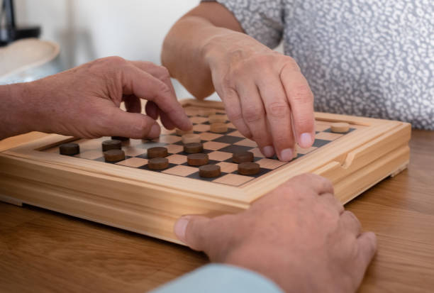 istock Two senior people at home while playing a game of checkers on wooden table. 1321117043