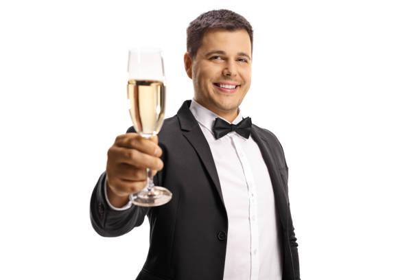 elegancki młody mężczyzna w garniturze i muszce tosty z kieliszkiem wina musującego - party business toast champagne zdjęcia i obrazy z banku zdjęć