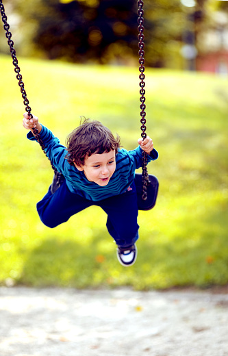 Portrait of a cute boy 5-6 years old  swinging on swing. Active leisure with kids. Happy boy.