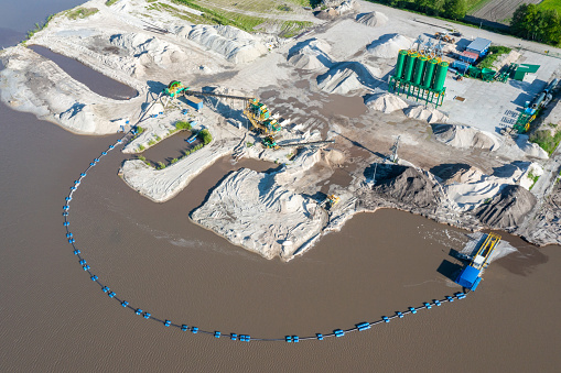 Aerial view of the open pit mine located by the water, machine for the extraction of crushed stone, green silos.