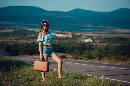 Young beautiful Asian woman in hippy style. travels by hitchhiking. Road in the mountains. The idea and concept of summer holidays and freedom
