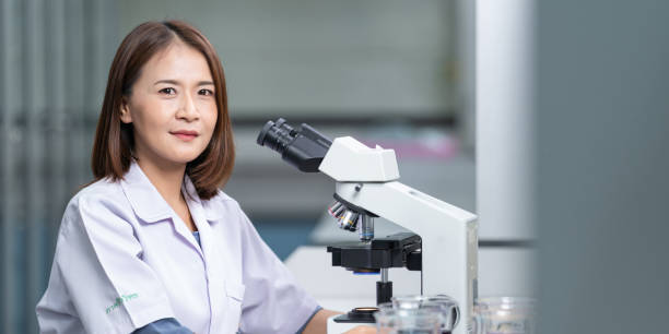 A young scientist woman in a laboratory coat looking through a microscope in a laboratory to do research and experiment. Scientist working in a laboratory stock photo