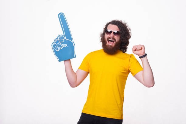 istock Amazed man with beard screaming and supporting his favorite sport team and pointing with fun glove 1321131360