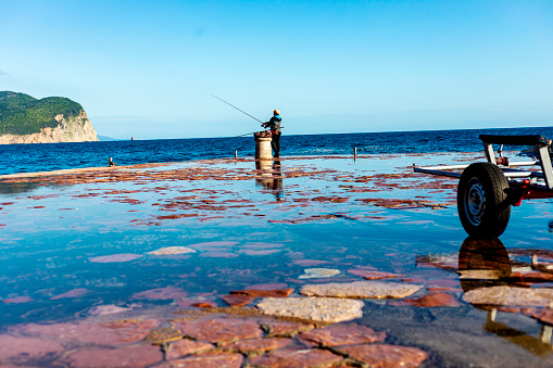 a photograph of a fisherman fishing from a dock in a small port
