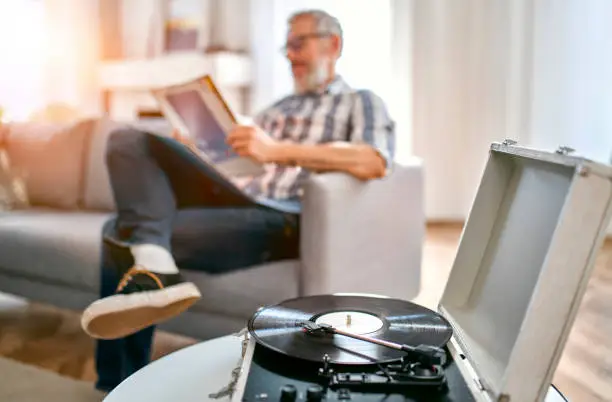 A mature man sits on the couch at home, relaxes, enjoys life and listens to vinyl records on a music player.Turntable playing vinyl LP record.