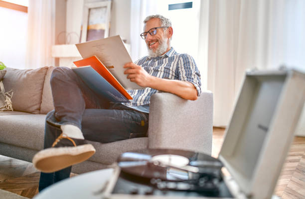 Mature couple at home A mature man sits on the couch at home, relaxes, enjoys life and listens to vinyl records on a music player.Turntable playing vinyl LP record. record analog audio stock pictures, royalty-free photos & images